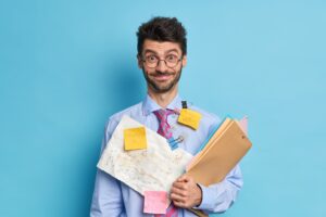 Cheerful bearded male financier prepares stratup project poses with papers and folders dressed in fo